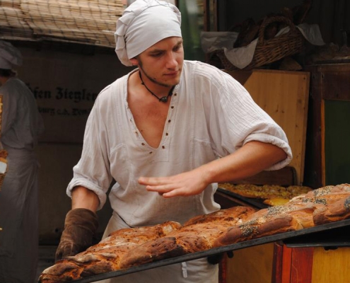 Ein Bäcker zieht ein Backblech mit frischem Brot aus dem Ofen