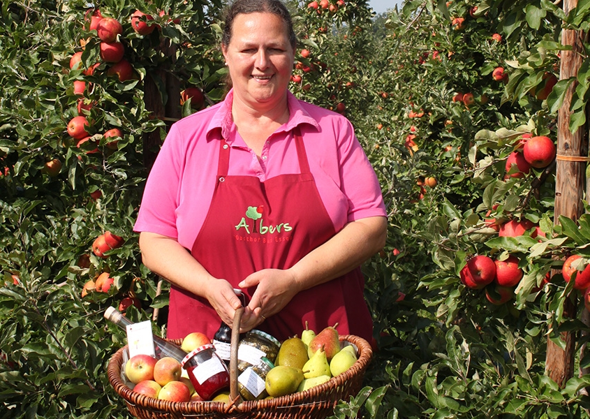 Verkäuferin mit Obst-Warenkorb zwischen Apfelbäumen